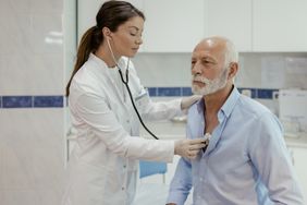 A doctor listens to an older man's lungs with a stethoscope