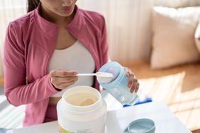 Young woman wearing pink sports coat scooping l-carnitine powder into a shaker bottle