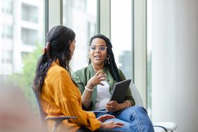 two neurotypical people sitting on chairs near a large window chatting with each other