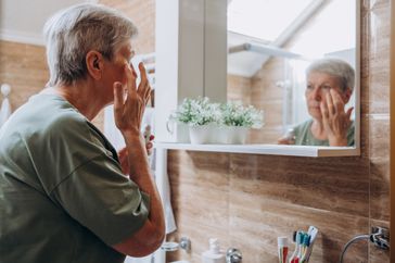 An older woman puts cream under her eyes