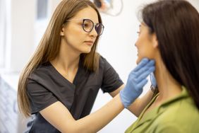 Dermatologist examines person's face in doctor office.