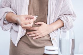 A person takes a pill with a hand on their stomach
