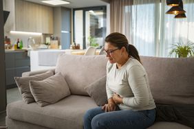 middle aged woman sitting on the cough holding her stomach due to abdominal pain