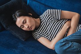 Person lays on couch holding abdominal area in discomfort.
