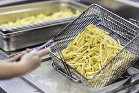 Someone holding a frying pan with french fries at a commercial kitchen.