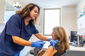 Nurse or nursing assistant giving female patient injection for flu vaccination campaign in a medical center to fight winter illnesses or infections