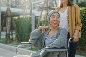 Young Asian woman cancer patient wearing a gray cardigan, gray beanie, is outside and sitting in a wheelchair. 