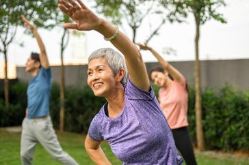 older woman in purple shirt dancing during zumba class in a park