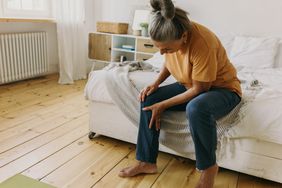older adult sitting on bed and grabbing her knee due to aches and pains