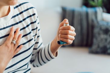 A woman holds her chest and inhaler during an asthma attack