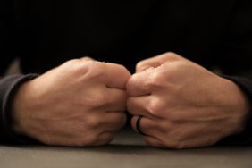 Frontal point of view, man's hands touching with their fists closed with a sense of reflection. Close-up image, near the dark surface.Dark background and unrecognizable person