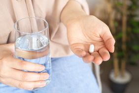 Woman with glass of water and pill on blurred background, closeup. Healthcare, medicine, treatment, therapy concept