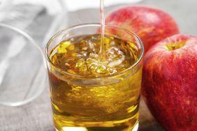 Pouring apple juice into a glass on a table with juicy red apples close up.