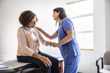 Nurse giving senior woman a joint exam in doctors office.