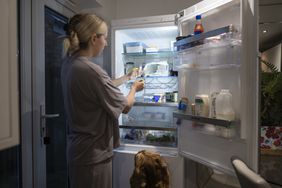 person placing ozempic in the middle shelf of an open refrigerator in the kitchen