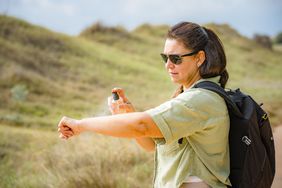Person applying mosquito repellant on their arm while on a park hike
