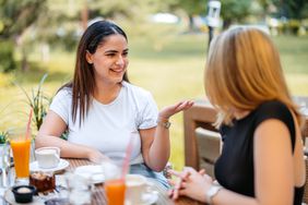 young woman sitting on a table outside talking to her friend who is actively listening 
