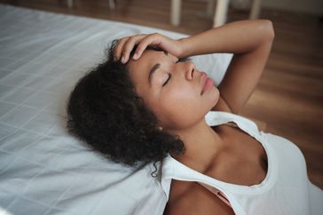 A tired woman closes her eyes and puts a hand on her head