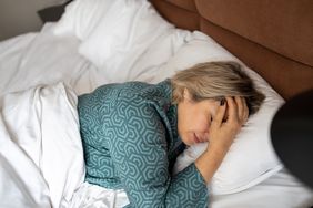Mature woman lying in bed covered with a blanket.