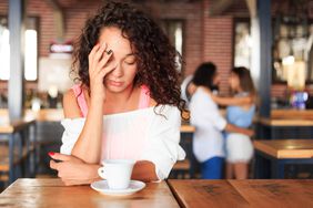 Person looks tired in front of coffee in a shop.