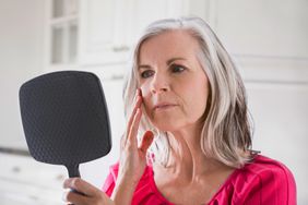 Caucasian woman looking at skin in mirror