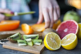 Close-up of sliced lemons, grapefruit, oranges, kiwi. Hands in the background, slicing an orange