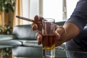 A person holding a cigarette and shot glass.