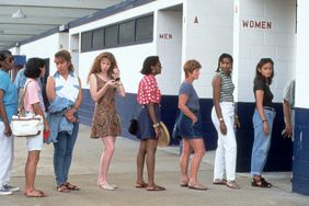 Long line of people stand outside a public restroom.
