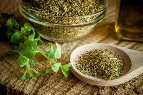 Dried oregano spice in a wooden spoon and glass bowl; fresh oregano sprig sits beside