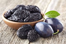 Wooden bowl full of prunes, with whole plums beside it