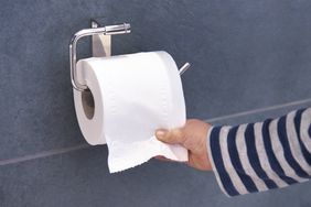 A person takes toiler paper from the toilet paper roll on the wall