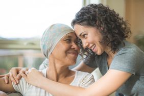 A young woman hugs her mom with cancer who's wearing a head covering