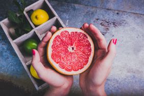 Hands holding a grapefruit sliced in half.