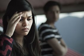 Close up of a person who looks upset with a blurry person in the background.