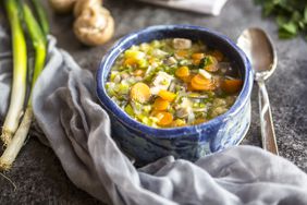 a blue bowl of soup with vegetables sitting atop a counter 