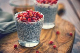 Two glass cups of chia seed pudding topped with pomegranate seeds, on a wood cutting board