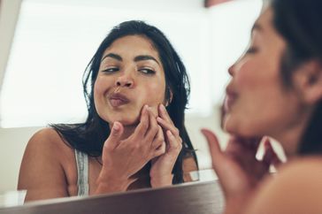 a woman looking at her face in the mirror
