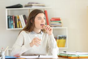 A teenage girl takes a supplement while doing her homework