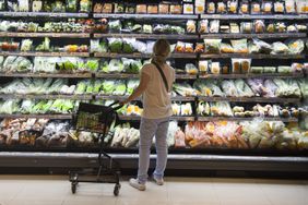 A shopper looks at shelves of vegetables wrapped in plastic. 