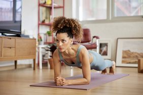 A young woman with curly hair doing plank in living room.
