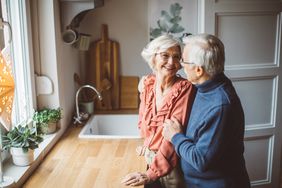 Senior couple for Christmas at home. They are standing in front of kitchen window and hugging.