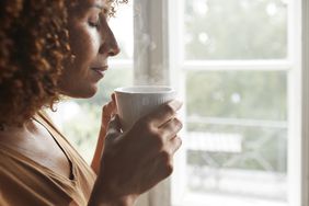 A woman drinking hot water by a window