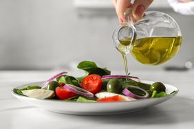 Woman pouring cooking oil onto plate with salad at white table