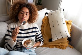 Woman eating healthy granola and yogurt breakfast sitting on the couch at home