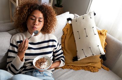 Woman eating healthy granola and yogurt breakfast sitting on the couch at home
