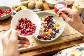 An older person's hands pouring pomegranate seeds into a yogurt bowl