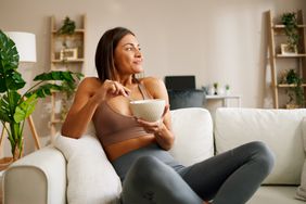 Young woman is sitting on the sofa in the living room and eating a high-protein, low-sodium snack