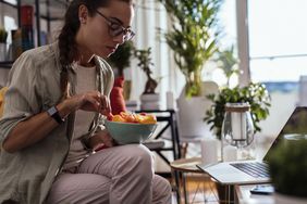 Young woman eating fruits while working in her living room