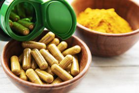 Turmeric powder and turmeric capsules on white wooden background