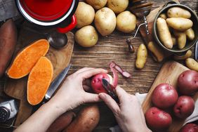 Hands peeling a mix of different potatoes in a wooden table